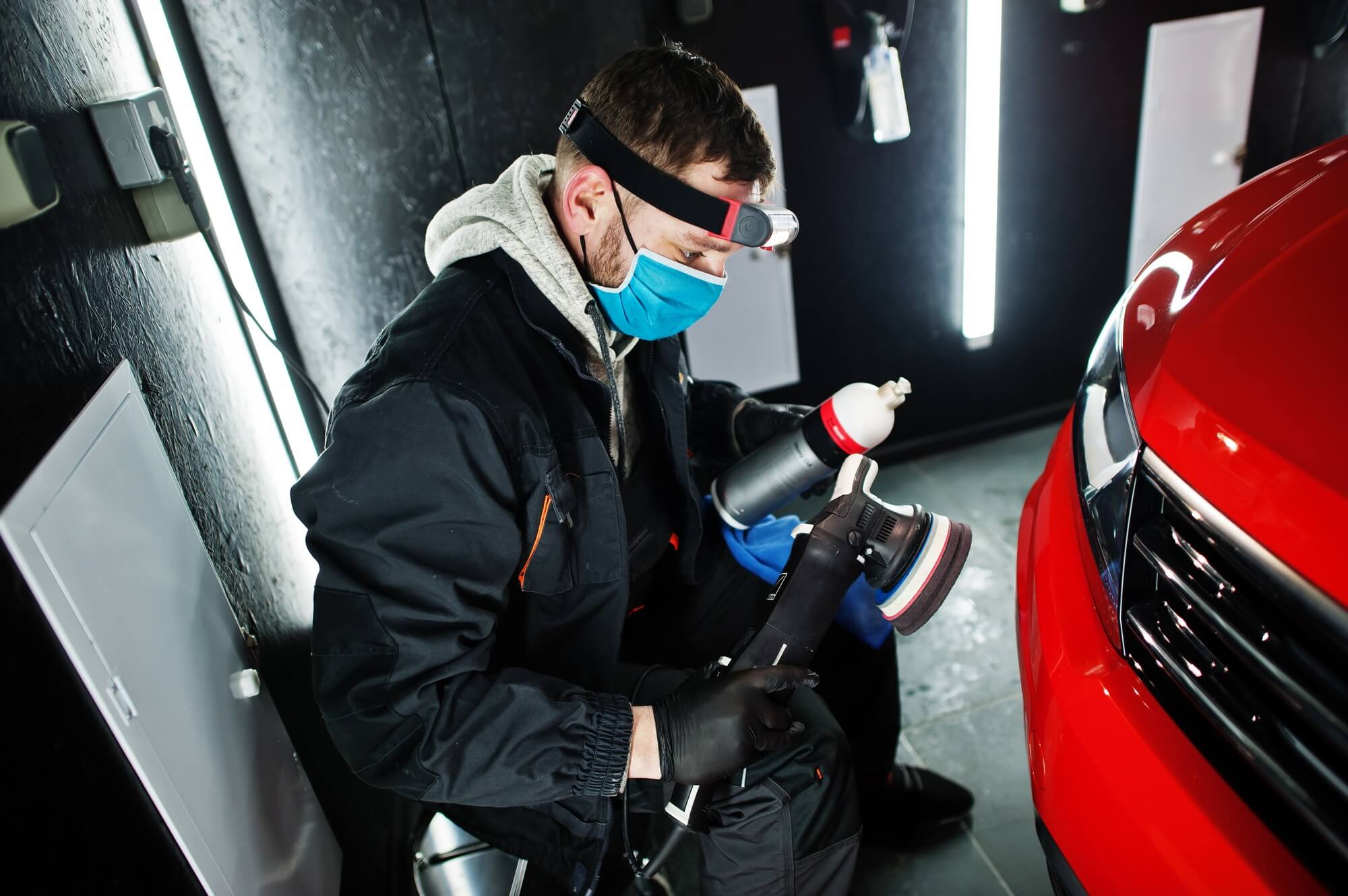 Professional detailer polishing a vehicle in a working shop